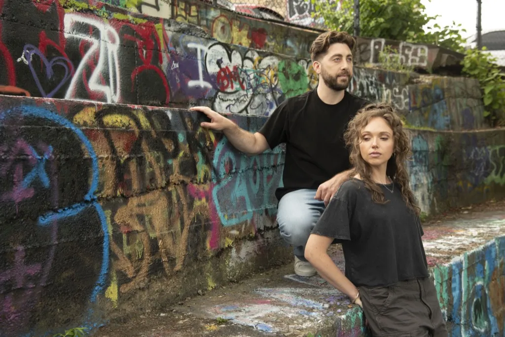 Schmarx and Savvy in front of a graffiti-covered wall