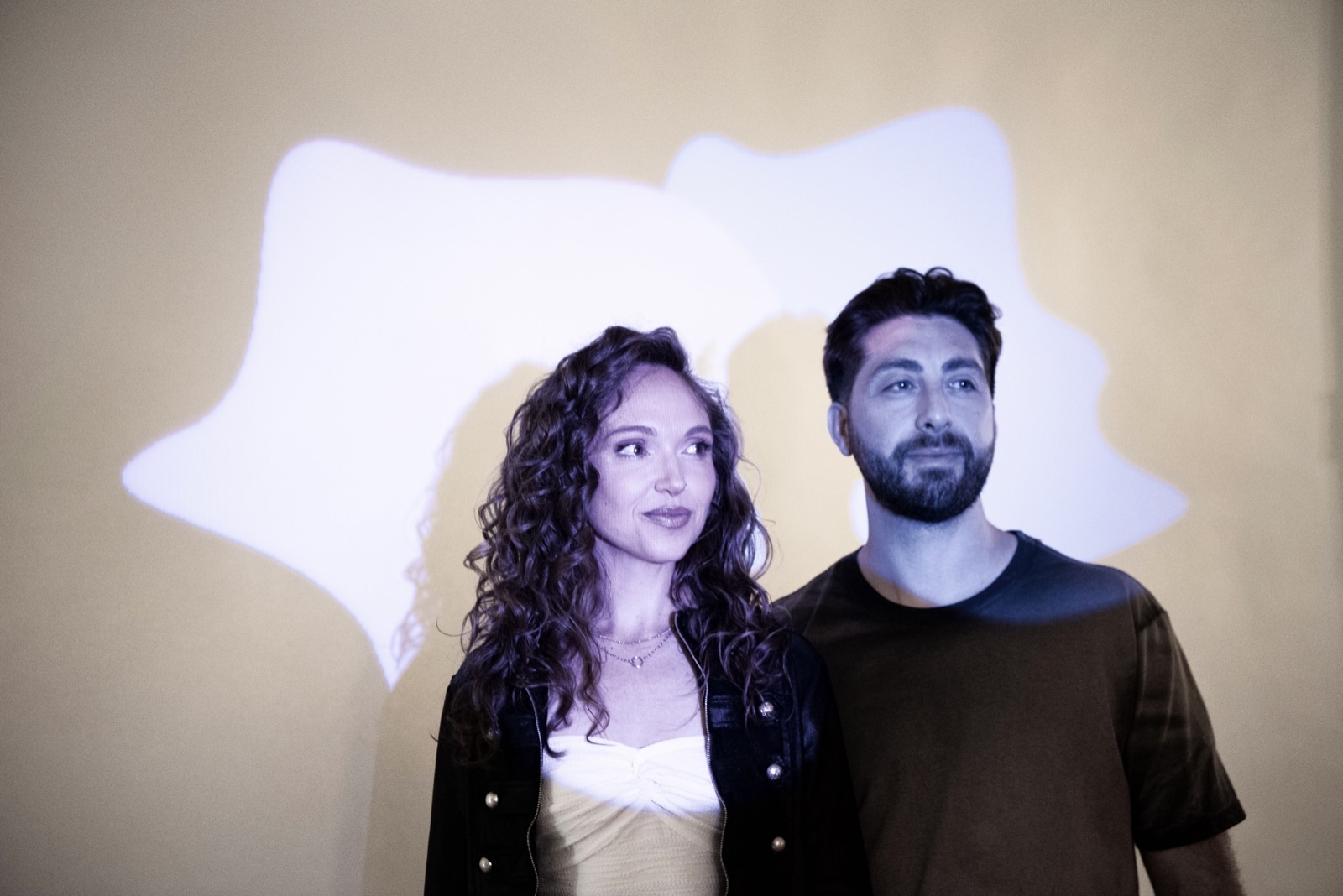 Schmarx and Savvy standing against a warm wall washed with projected light